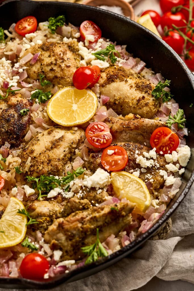 Juicy lemon greek chicken thighs cooked in a skillet, garnished with cherry tomatoes, fresh parsley, and lemon slices for a flavorful, healthy meal.