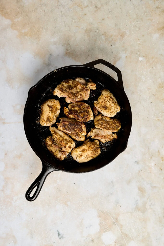 Juicy grilled chicken thighs cooking in a cast iron skillet, perfect for flavorful and tender meal preparation.