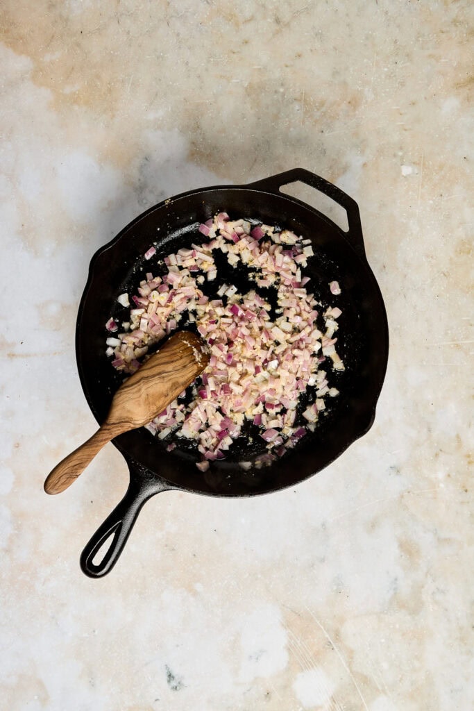 Sautéed chopped onions in a black cast iron skillet with a wooden spoon, ready for cooking or serving.