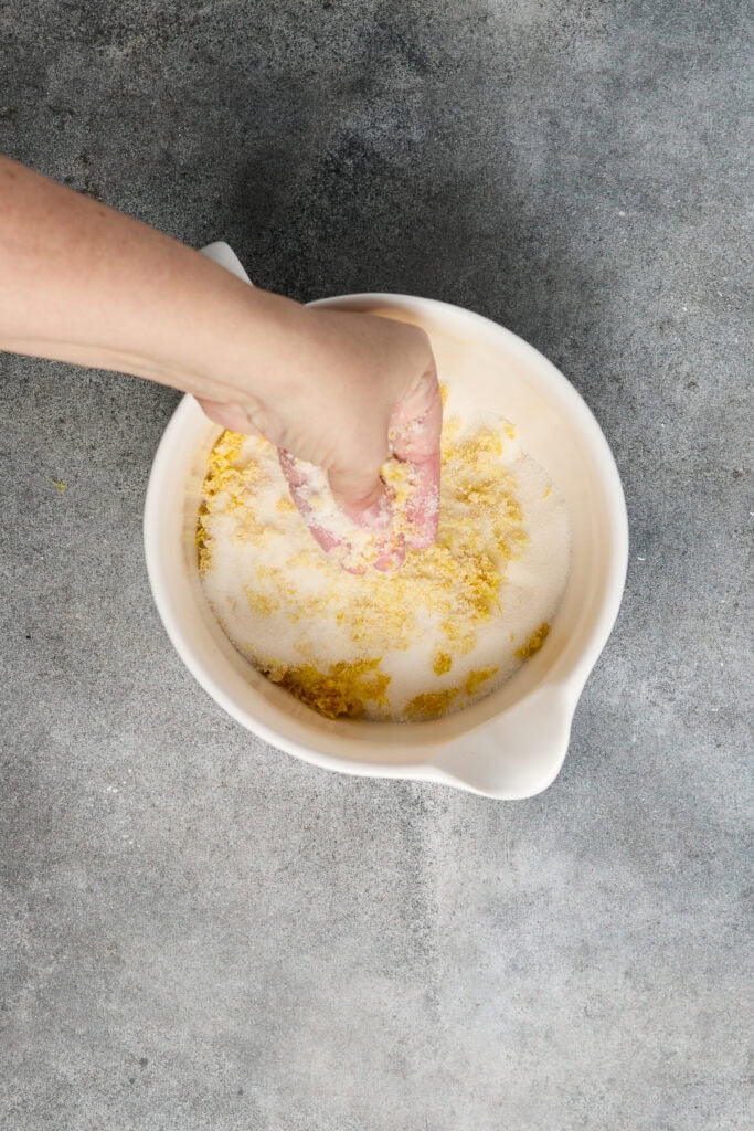 Hand mixing lemon bar ingredients in a bowl, showcasing the process of making fresh lemon bars for dessert.