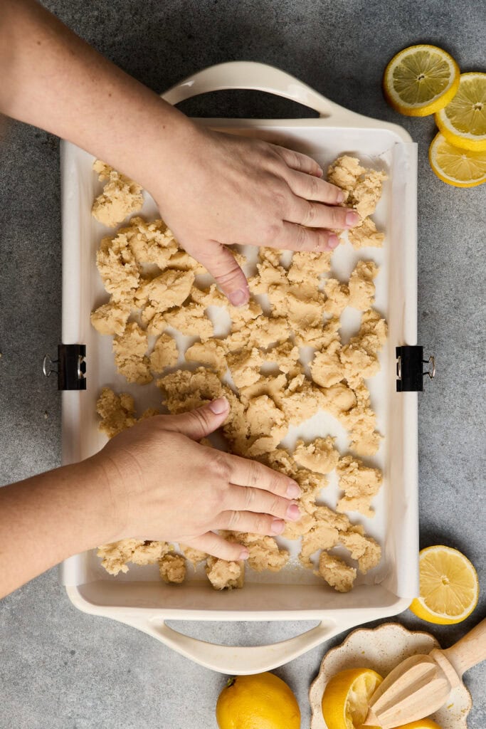 Hands pressing lemon sugar cookie dough in a baking tray with fresh lemon slices around, ready for baking.