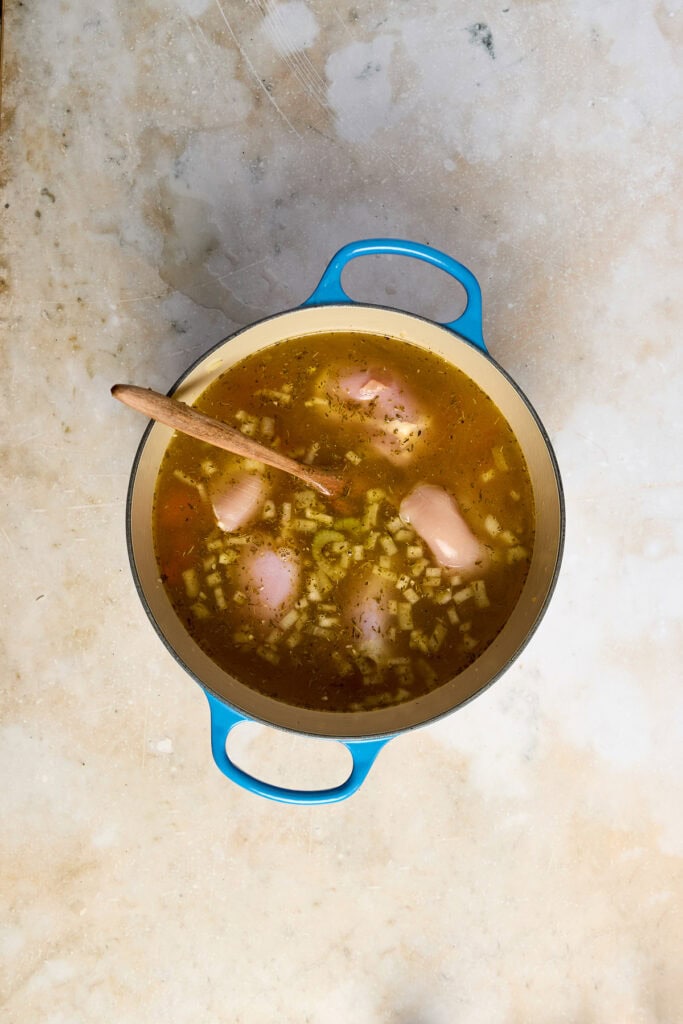 Warm lemon chicken rice soup in a blue pot with a wooden spoon, featuring tender chicken pieces and rice in a flavorful broth. Perfect comfort food for cold days.