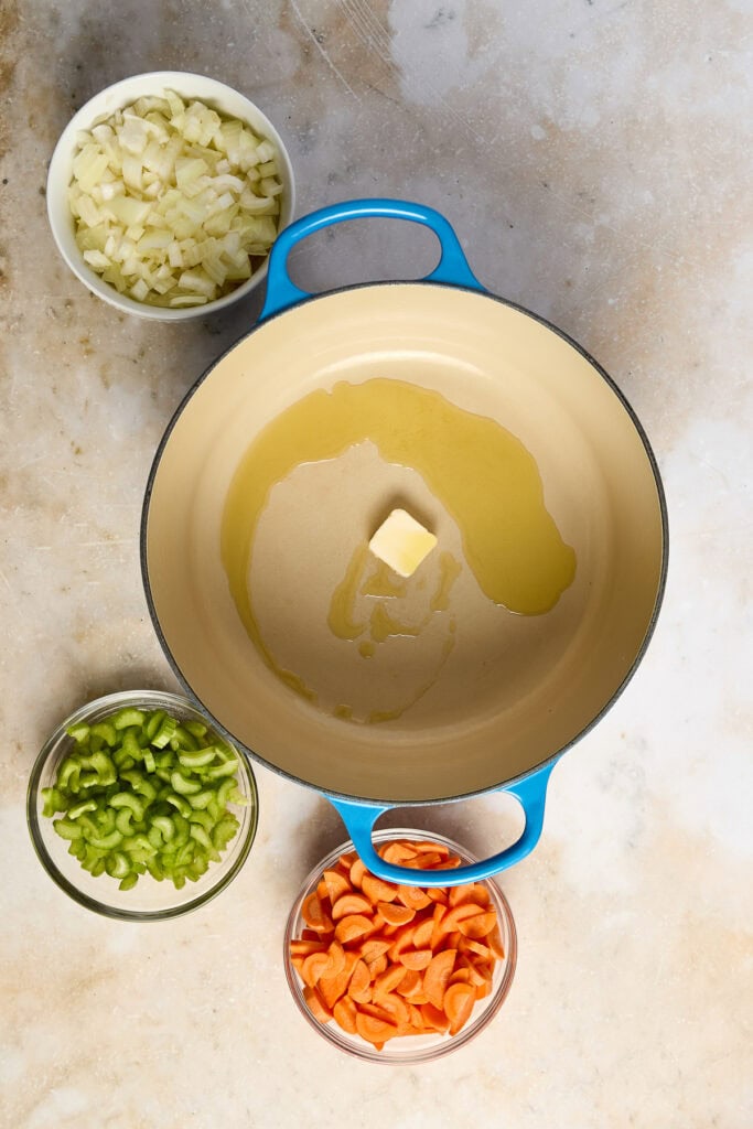 Ingredients for Lemon Chicken Rice Soup, including chopped onions, celery, carrots, and butter in bowls with a soup pot.