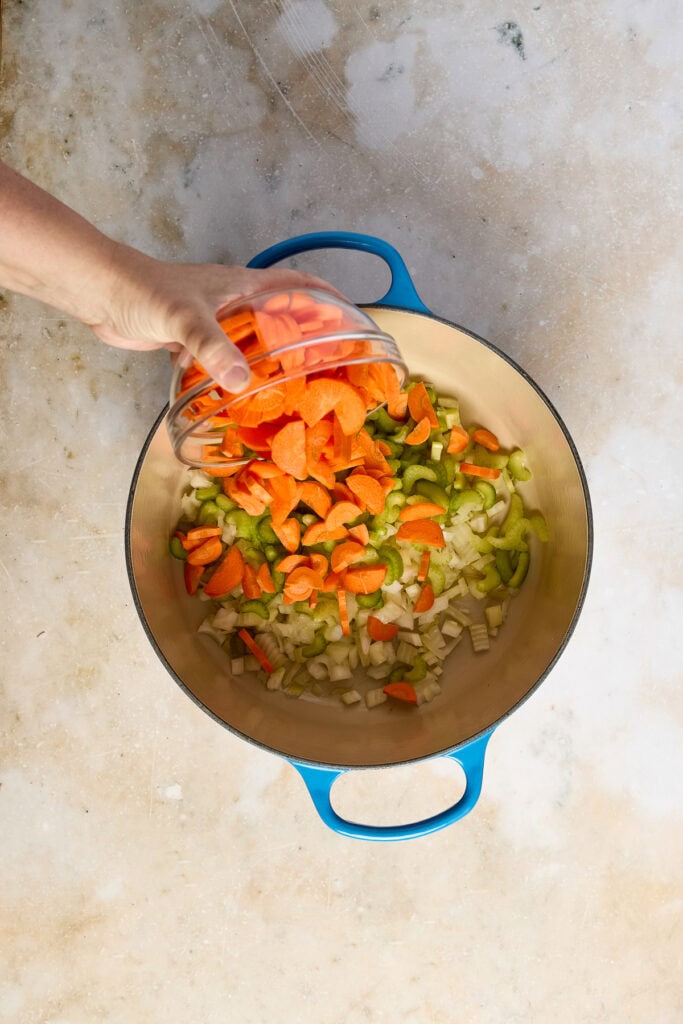 Fresh chopped carrots and celery in a blue pot for Lemon Chicken Rice Soup preparation.