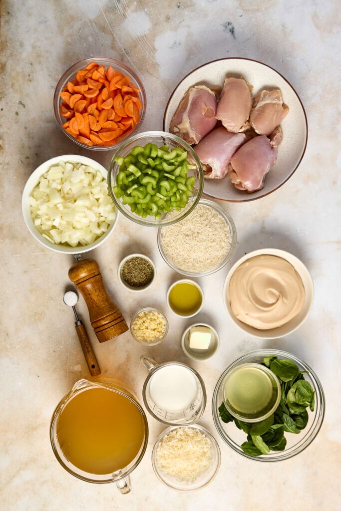 A delicious collection of fresh ingredients for Lemon Chicken Rice Soup, including chicken, carrots, celery, onion, rice, lemon, and herbs, arranged on a neutral background.