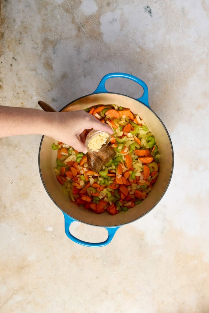 Hand adding lemon to a pot of cooked vegetables for lemon chicken rice soup, showcasing fresh ingredients and cooking process.