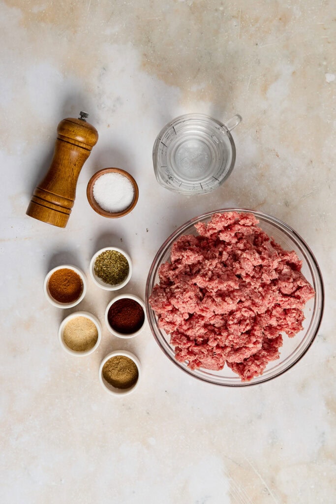 Ground meat mixture with spices and salt in a glass bowl, ready for cooking or baking, on a textured surface.