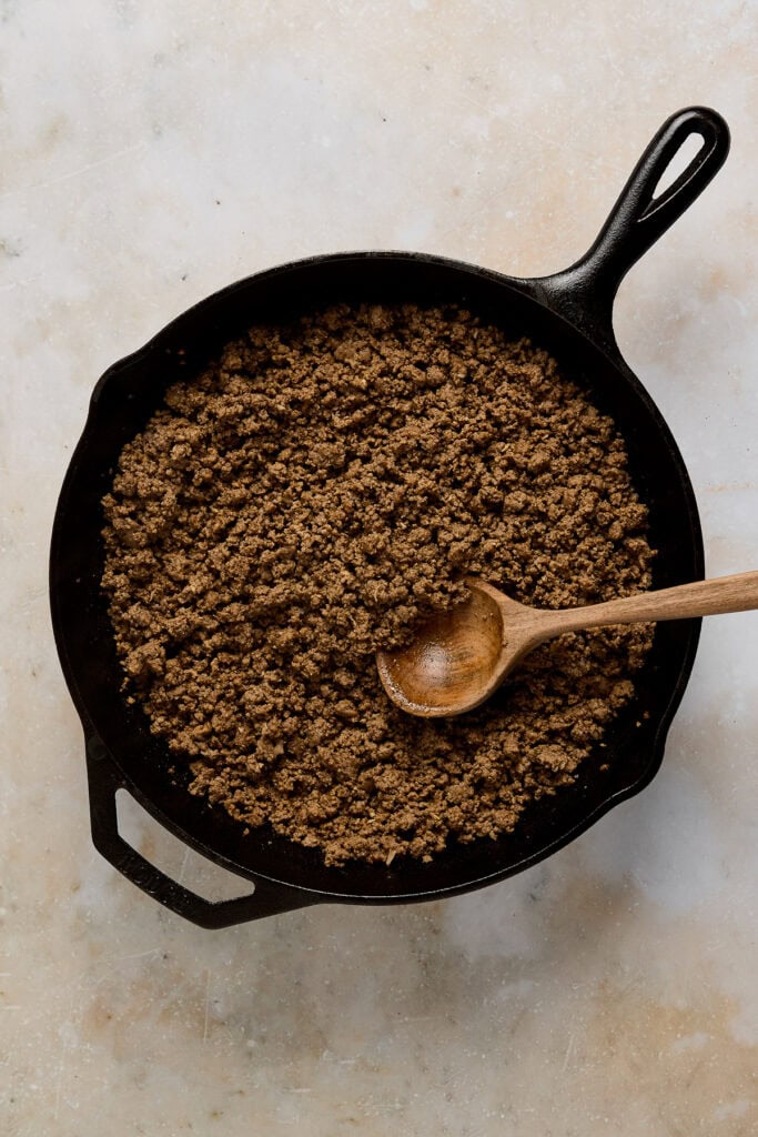 Close-up of sweetened ground cinnamon in a cast iron skillet with a wooden spoon, perfect for baking and dessert recipes.