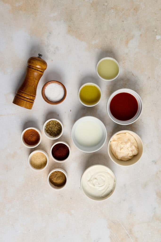 Assorted sauces, spices, and condiments arranged on a neutral surface, including mayonnaise, ketchup, mustard, olive oil, and various seasonings, ideal for baking and cooking.