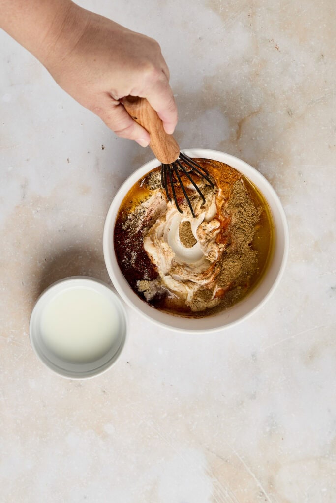 Delicious cake batter being prepared with a whisk in a white bowl, accompanied by a glass of milk, perfect for baking sweet treats.