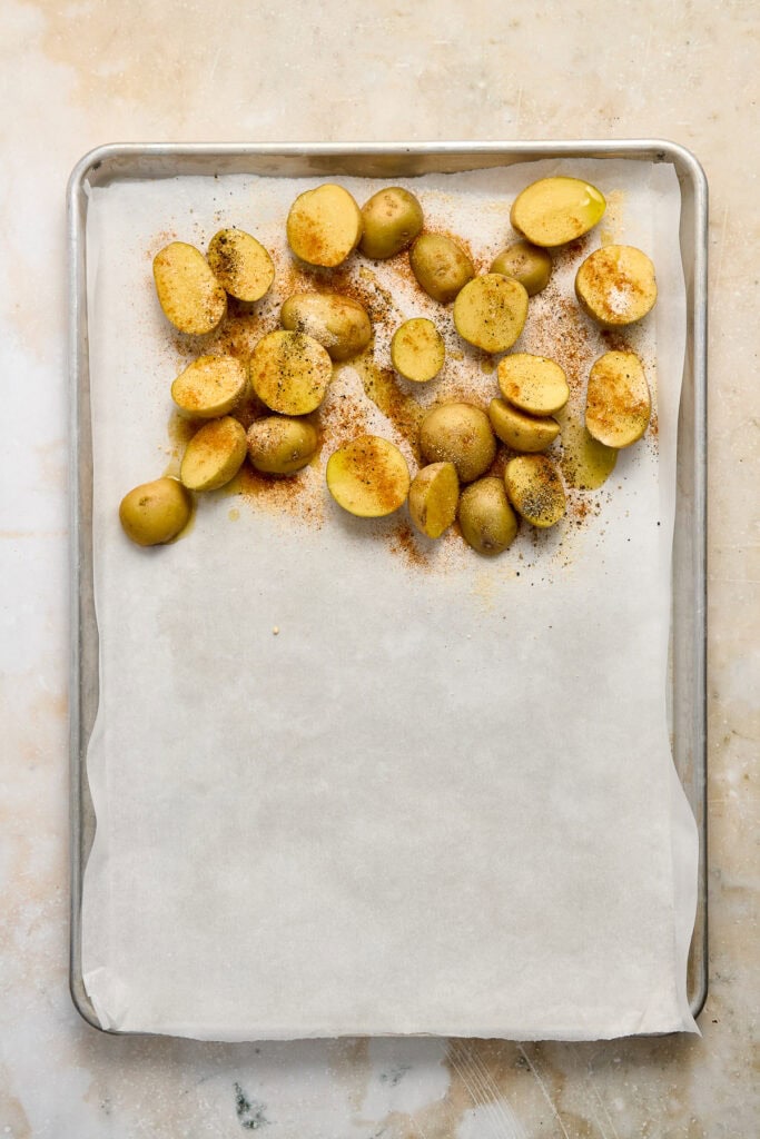 Golden roasted baby potatoes on baking sheet with seasoning and spices.