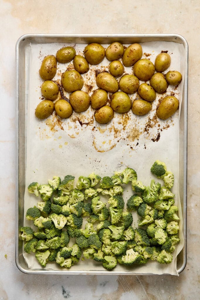Roasted baby potatoes and broccoli on a baking sheet, seasoned with herbs and spices, ready for a healthy meal or side dish. Perfect for vegetable lovers and nutritious recipes.