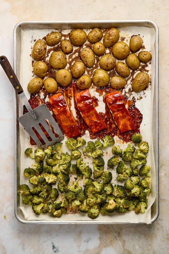 Delicious roasted potatoes, barbecue salmon, and seasoned broccoli florets arranged on a baking sheet, perfect for a hearty, healthy meal or side dish.