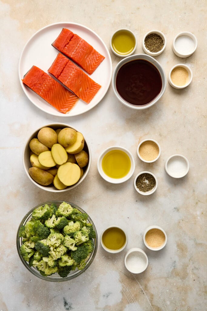 Fresh salmon fillets, broccoli, potatoes, and various seasonings with olive oil and spices.