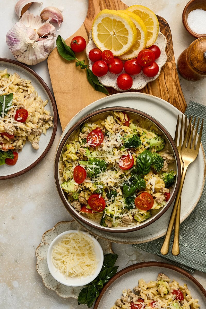 Garlic parmesan orzo with cherry tomatoes, basil, and grated cheese on a rustic wooden table.