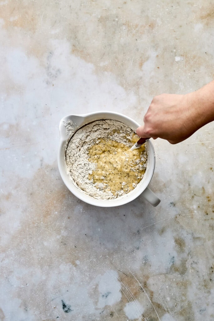 Hand mixing cookie dough in a white bowl on a textured surface, showcasing the process of preparing fresh cookie batter for baking.