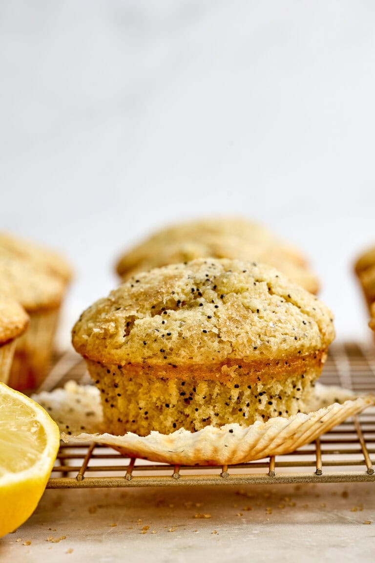 Freshly baked lemon poppy seed muffin with a golden crust, placed on a cooling rack with lemon slices nearby, showcasing a delicious homemade bakery treat.