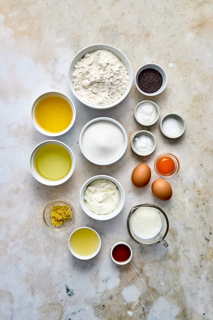 Assorted baking ingredients including flour, eggs, sugar, butter, and flavorings arranged on a rustic surface for baking preparation.