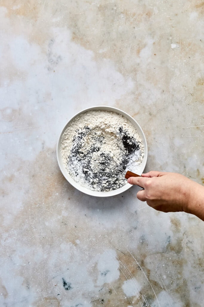 Close-up of cookie dough in a white bowl with chocolate chips, on a textured beige surface, ready for baking.