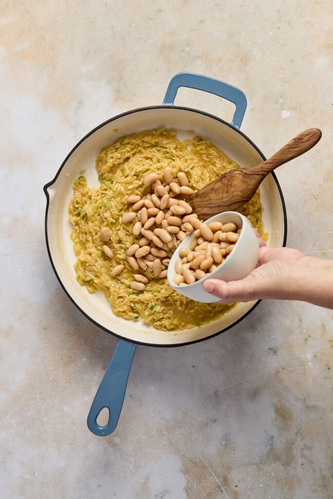 Close-up of creamy spinach feta orzo with white beans in a skillet, ready to serve, on a neutral background.