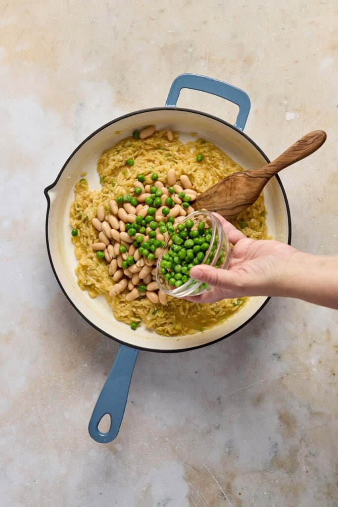 Delicious spinach feta orzo dish topped with white beans and fresh lemon, served in a skillet. Perfect for a healthy, flavorful meal with vibrant green peas and creamy feta cheese.