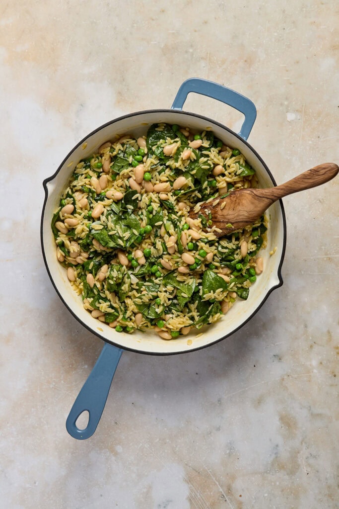 Healthy spinach and white bean dish in a skillet with a wooden spoon, perfect for nutritious meals.