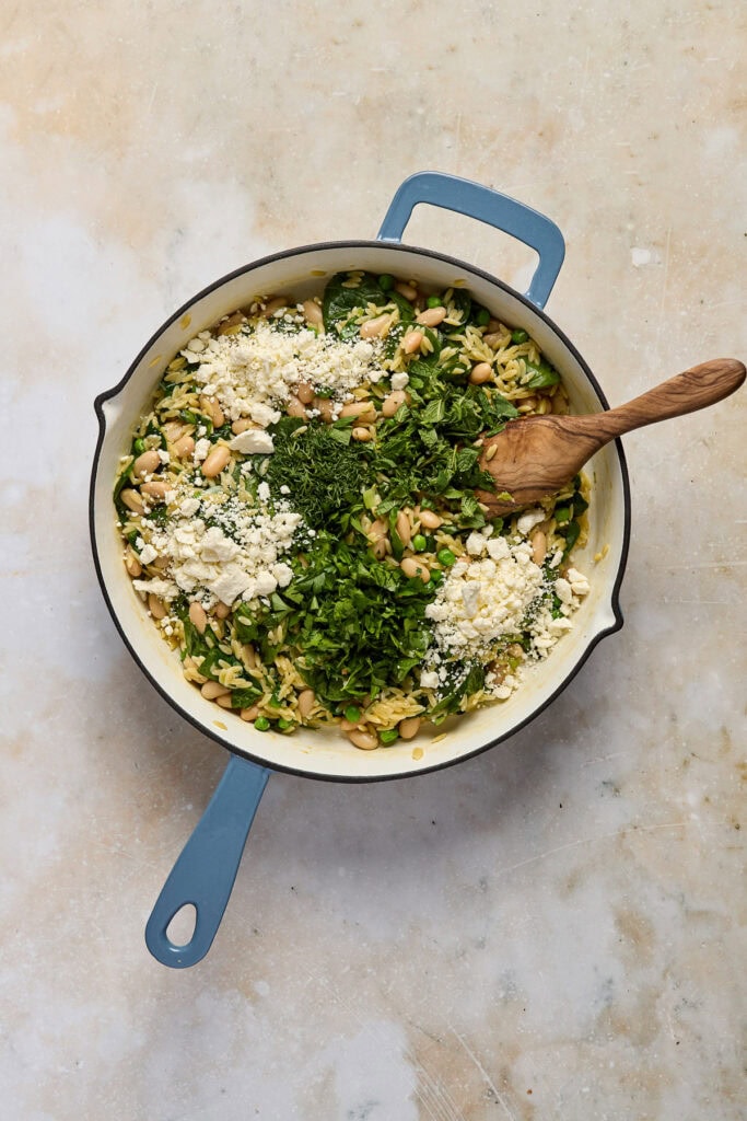 Spinach pasta dish with fresh greens, pine nuts, and cheese in a skillet, perfect for healthy meals.