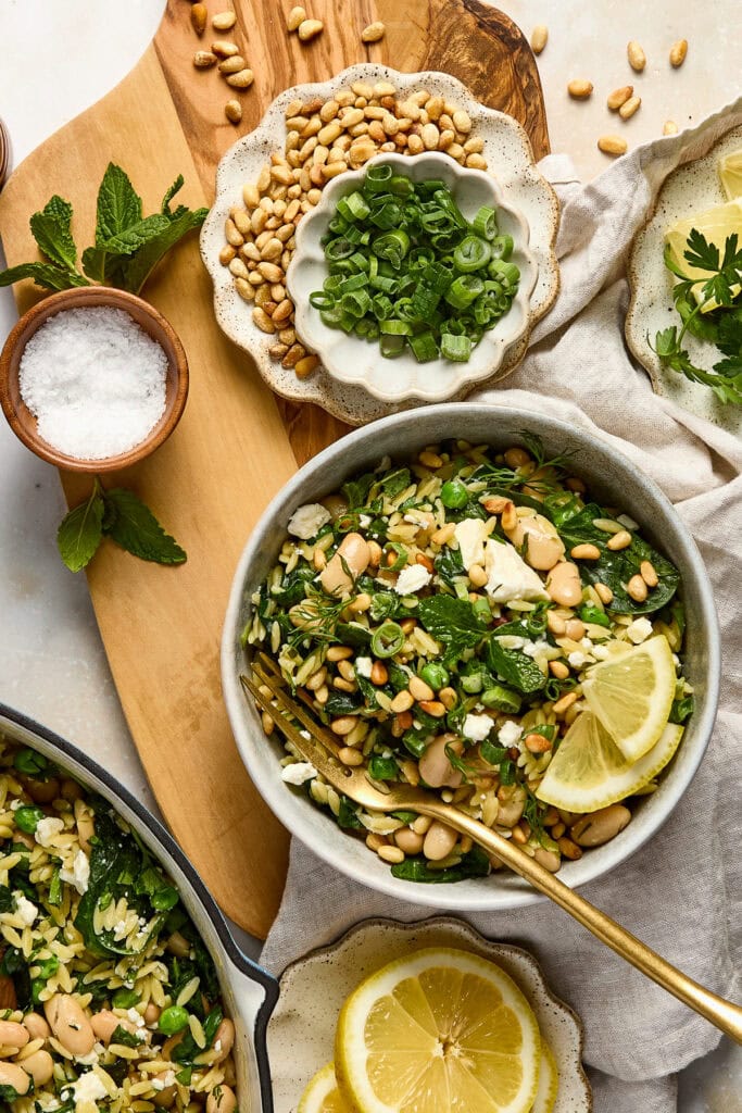 Healthy orzo salad with spinach, pine nuts, chopped green onions, and lemon slices, served in a rustic bowl. Perfect for a nutritious, flavorful meal or side dish.