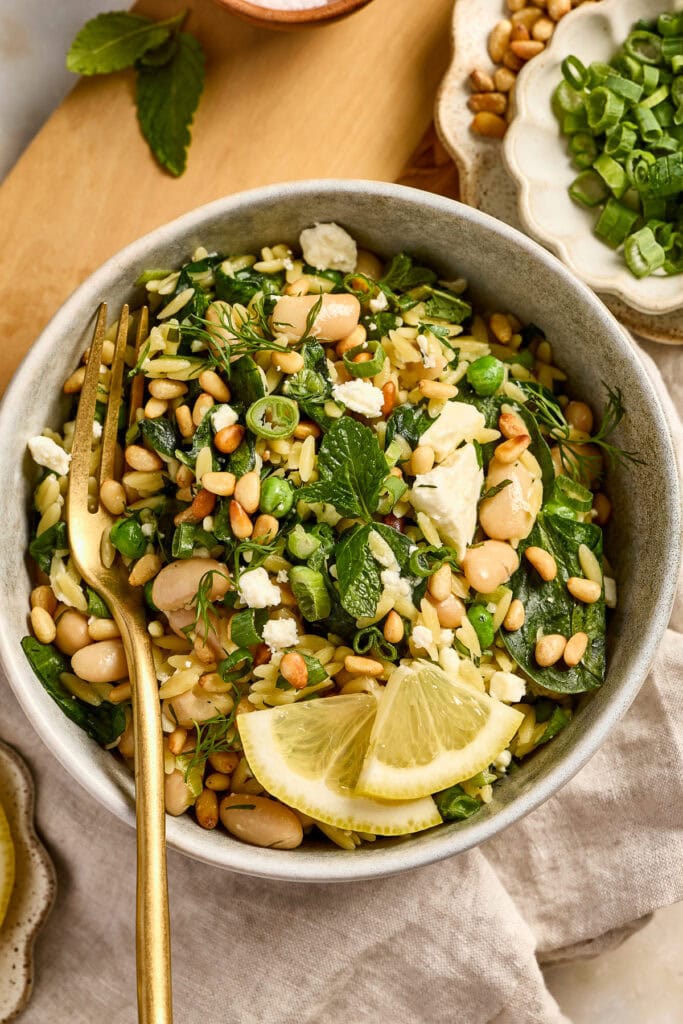 spinach feta orzo - Fresh spinach and white bean salad garnished with lemon wedges, topped with crumbled cheese and chopped green onions, perfect for healthy eating.