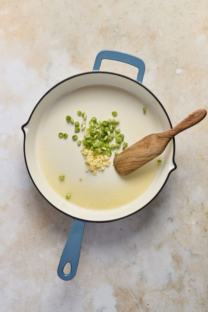 Creamy spinach feta orzo with white beans and lemon in a skillet, garnished with chopped green onions, served in a blue skillet on a neutral background.