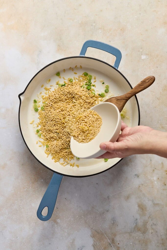 Delicious spinach feta orzo being cooked in a skillet with white beans and fresh lemon, garnished with chopped green onions. Perfect for a healthy, flavorful meal.