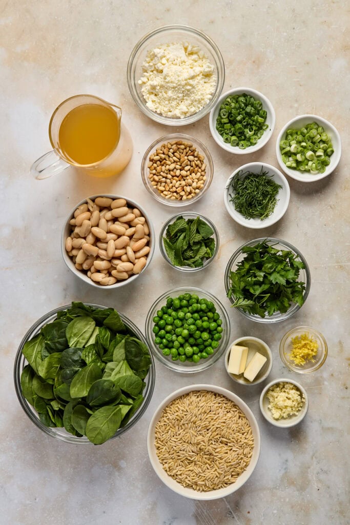 Fresh spinach leaves, chopped green onions, chopped herbs, pine nuts, grated cheese, butter, rice, and dressing ingredients for spinach-based recipes.