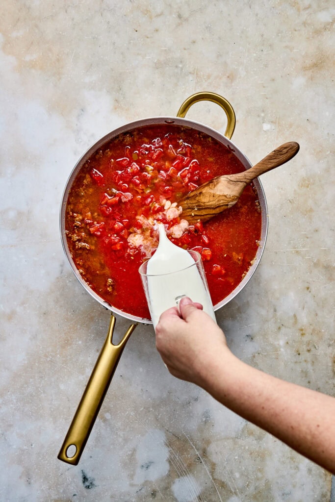 Close-up of cream being poured into a mixture of ground beef and tomato sauce to create taco pasta.