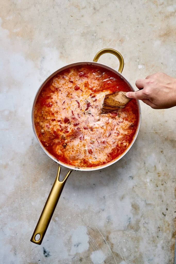 Taco pasta being stirred with a wooden spoon in a gold skillet. 
