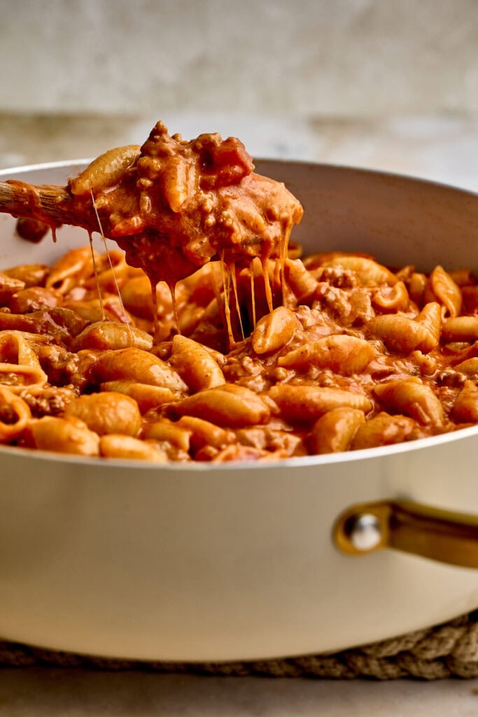 Close-up of a ground beef taco pasta with melted cheese in a white skillet, showcasing a hearty and flavorful comfort food dish.