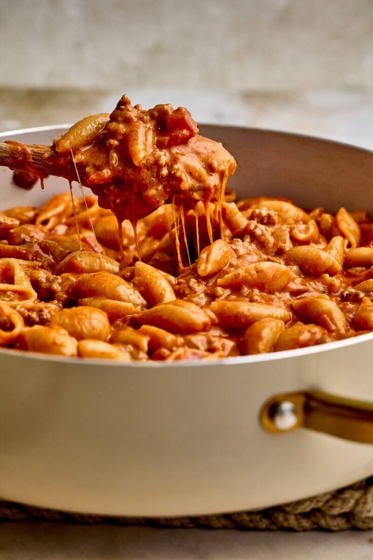 Close-up of a ground beef taco pasta with melted cheese in a white skillet, showcasing a hearty and flavorful comfort food dish.