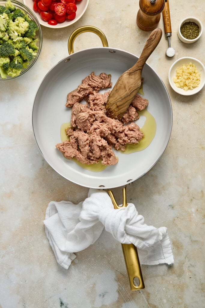Raw ground meat in a white skillet with olive oil, surrounded by fresh vegetables and spices, ready for cooking. Perfect for recipes like meat sauces, tacos, or casseroles.