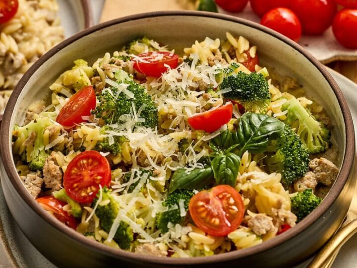Fresh vegetable pasta salad with cherry tomatoes, broccoli, and grated Parmesan cheese, served in a bowl with lemon slices and garlic in the background. Perfect for healthy, flavorful meals.