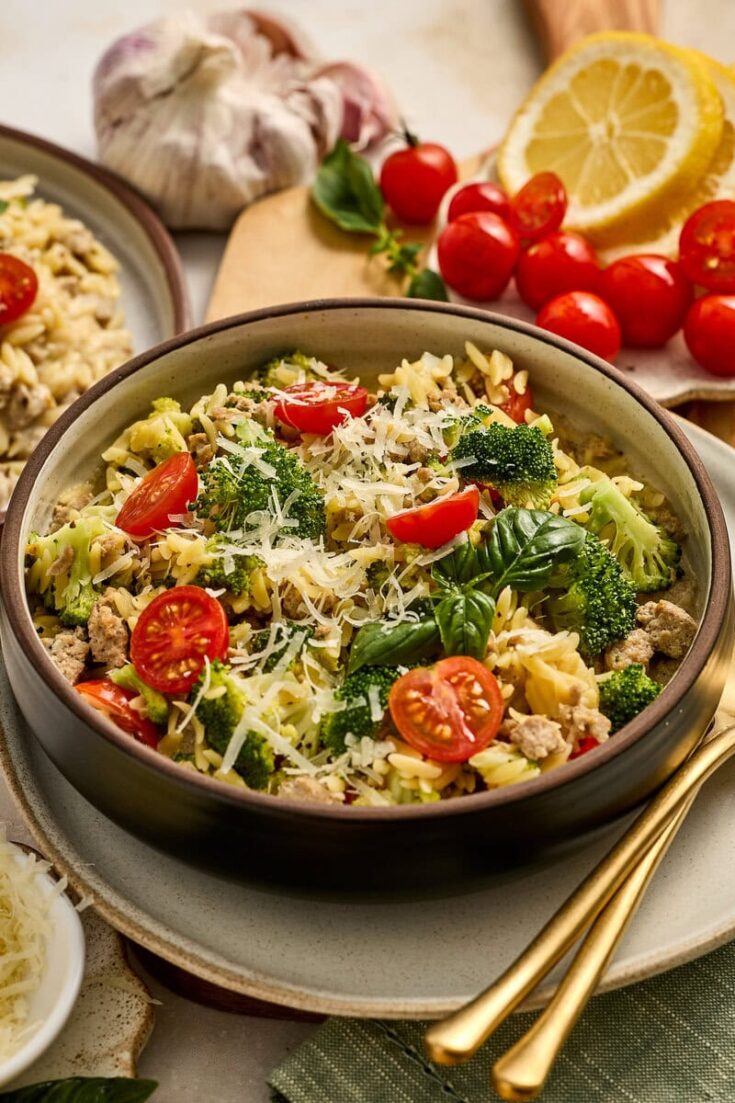 Fresh vegetable pasta salad with cherry tomatoes, broccoli, and grated Parmesan cheese, served in a bowl with lemon slices and garlic in the background. Perfect for healthy, flavorful meals.
