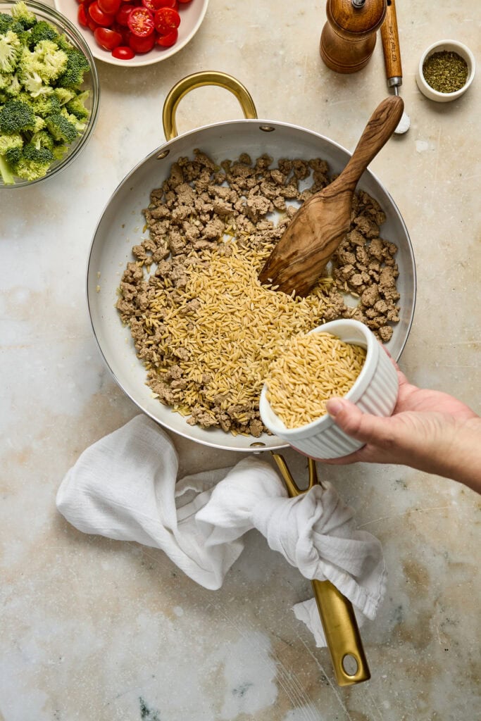 Cooking ground beef with cheese in a skillet, surrounded by fresh vegetables and spices, perfect for easy family dinners.