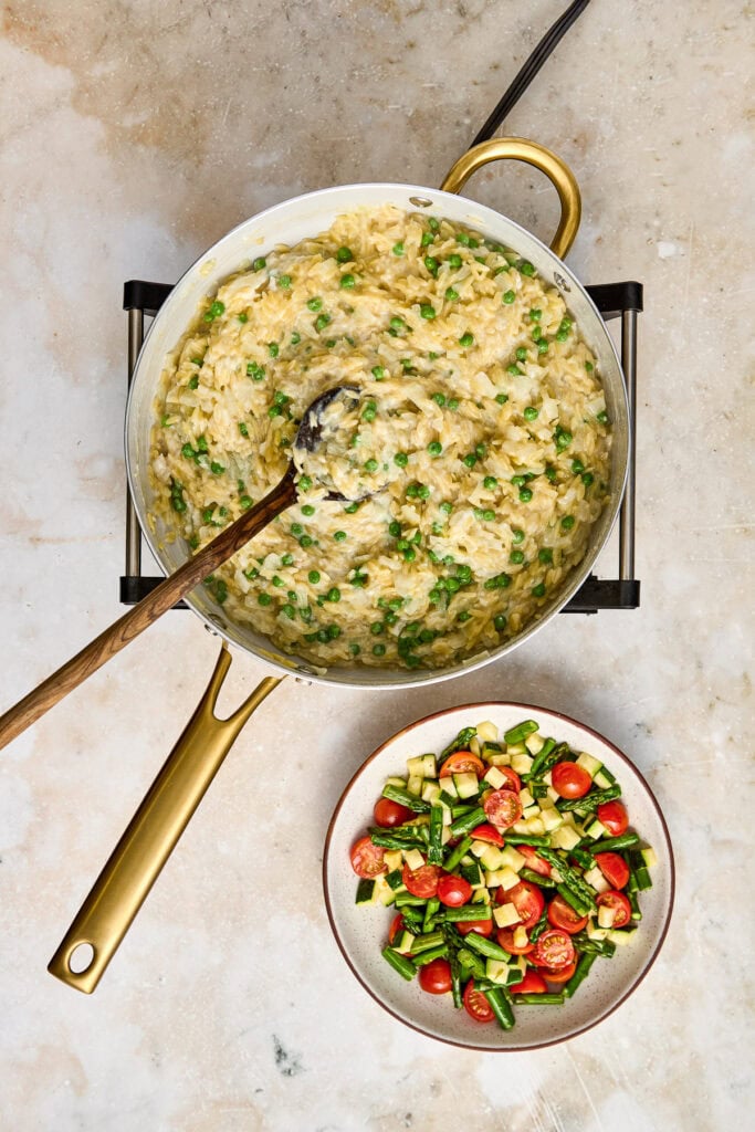 Creamy mashed potatoes mixed with chopped green onions in a white pot, served with a side of fresh vegetable salad featuring cherry tomatoes, cucumbers, and herbs.