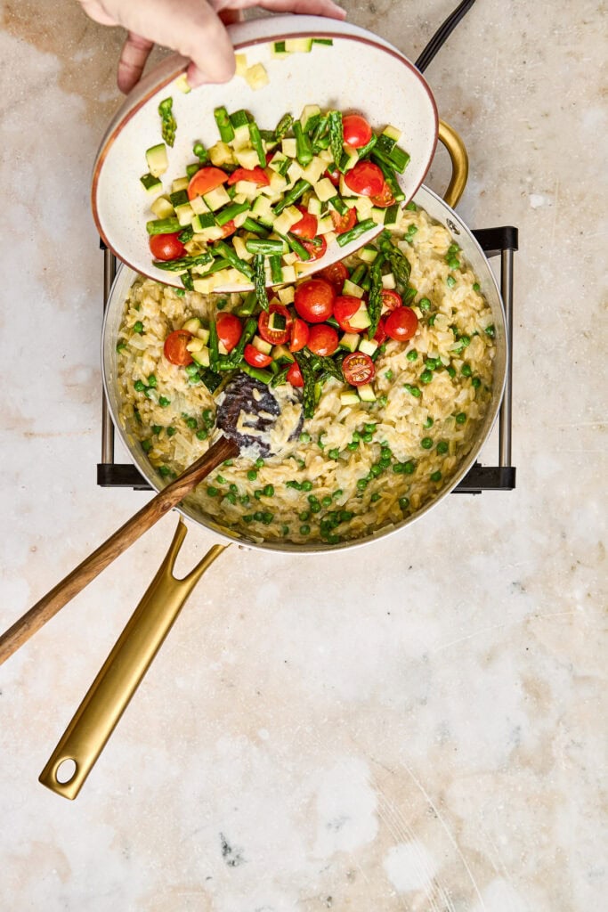 A skillet of creamy vegetable risotto topped with fresh cherry tomatoes and chopped green herbs, ready to serve.