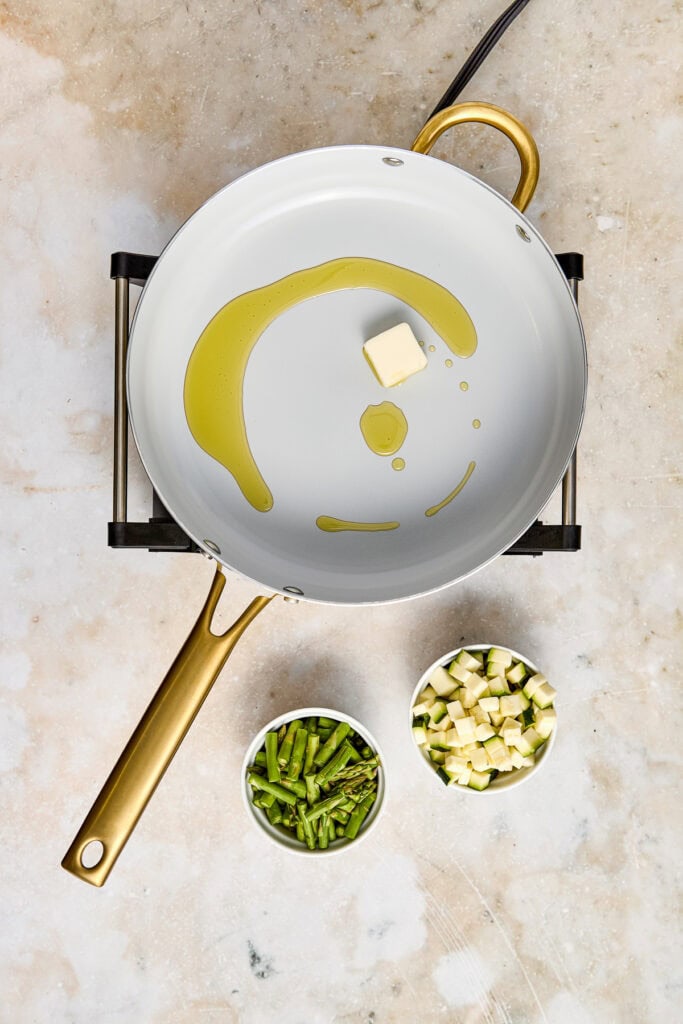 Close-up of butter melting in a white skillet with fresh chopped herbs and zucchini on the side, ready for cooking. Perfect for healthy recipes and flavorful dishes.