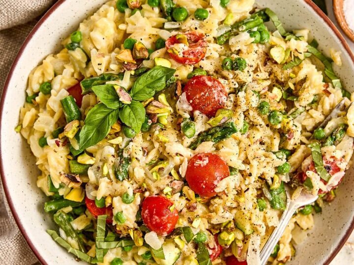 Colorful primavera orzo with cherry tomatoes, fresh basil, and chopped vegetables, served in a rustic bowl with herbs and seasonings, perfect for summer meals.