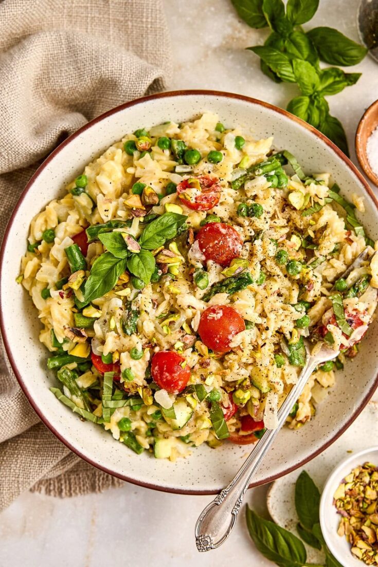 Colorful primavera orzo with cherry tomatoes, fresh basil, and chopped vegetables, served in a rustic bowl with herbs and seasonings, perfect for summer meals.