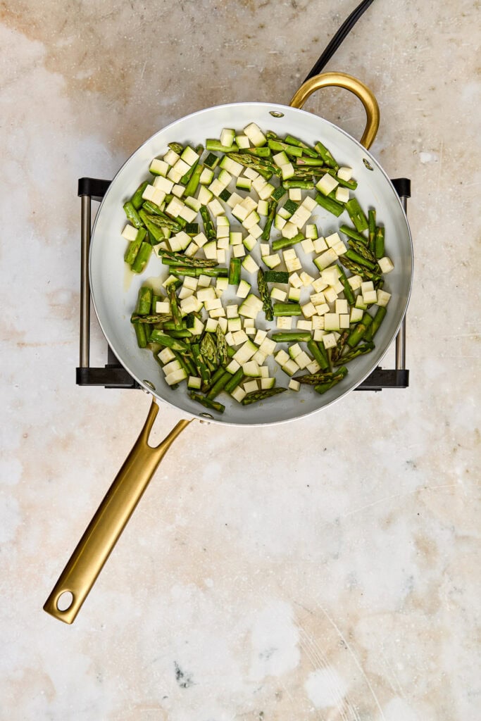 Sliced green onions and garlic in a white skillet with a gold handle, prepared for cooking.