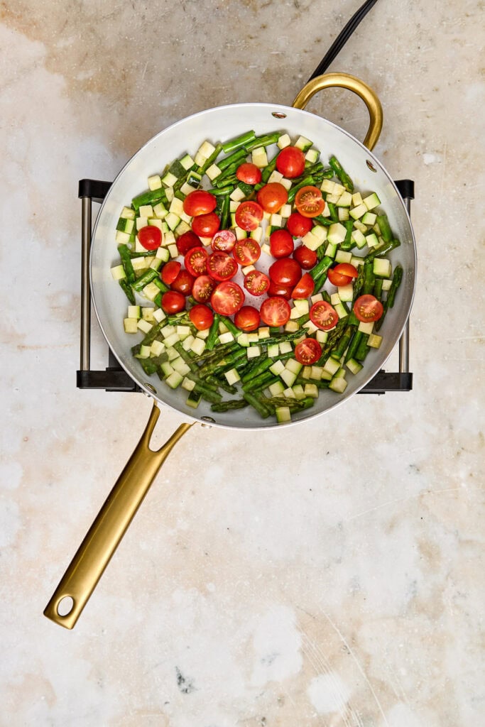 Bright cherry tomatoes and diced cucumbers in a skillet, ready for cooking or salad preparation.