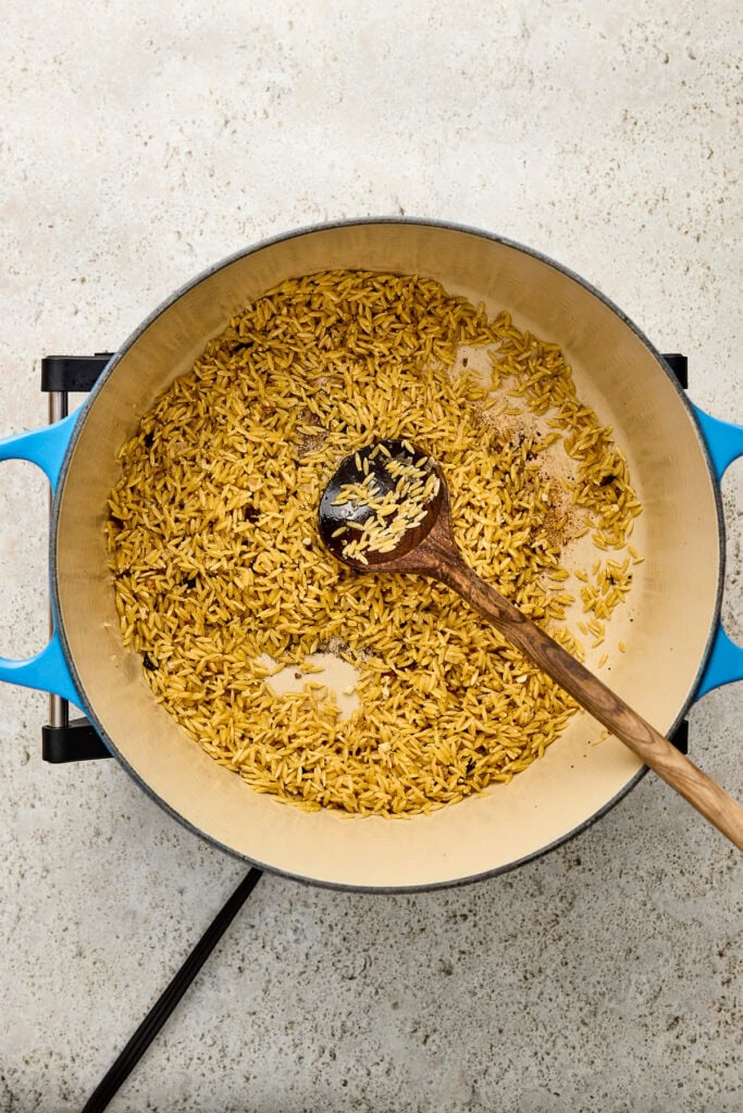 Saffron-infused pasta cooking in a blue skillet with a wooden spoon, showcasing a vibrant yellow color and creamy texture, perfect for gourmet dishes and culinary presentation.