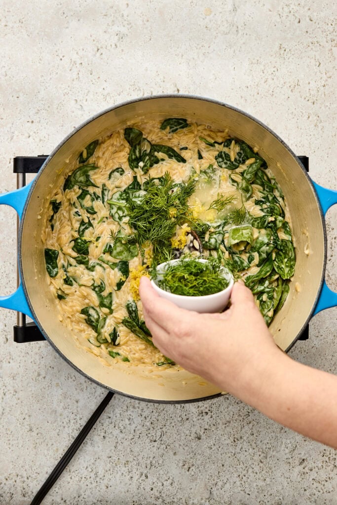 Cooking a creamy spinach and herb chicken dish in a skillet, with fresh herbs and greens being added for flavor and nutrition.