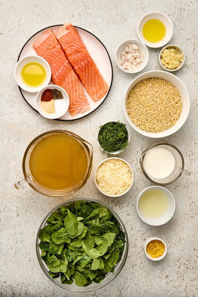 Fresh salmon fillets with rice, greens, and seasonings on a light countertop, ready for cooking a nutritious and delicious meal.